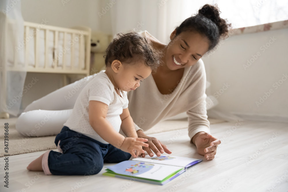 Smiling young african American mother sit on warm floor play with little infant toddler child, happy biracial mom relax have fun read book with small baby girl at home, motherhood, childcare concept Smiling young african American mother sit on warm floor play with little infant toddler child, happy biracial mom relax have fun read book with small baby girl at home, motherhood, childcare concept
