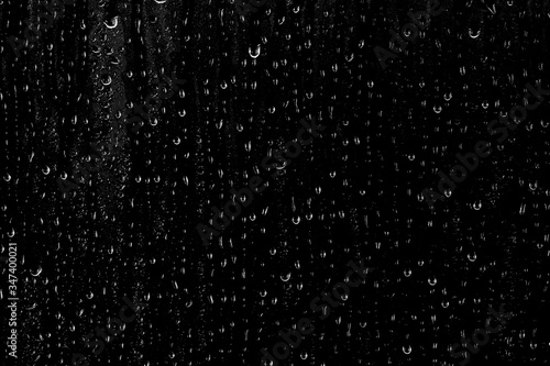 Drops of water flow down the surface of the clear glass on a black background. 