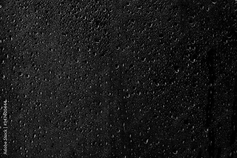 Drops of water flow down the surface of the clear glass on a black background.	