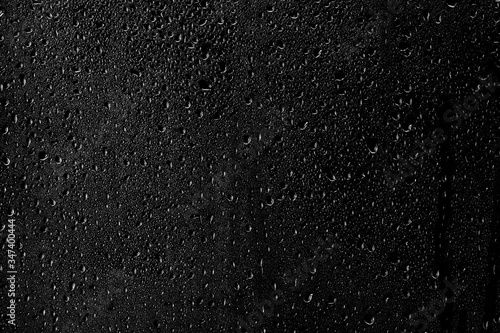 Drops of water flow down the surface of the clear glass on a black background.	