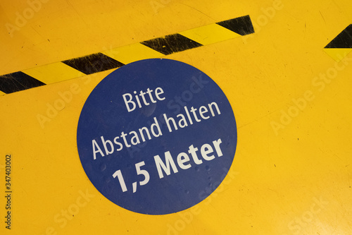 Ein Schild auf dem Boden mit Absperrband auf dem in Deutsch steht, dass man einen Abstand von 1,5 Metern halten soll