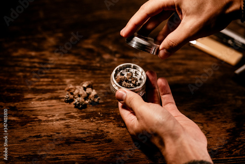 Two hands using a marihuana grinder to shred the buds before rolling a cannabis joint during Covid 19 crisis