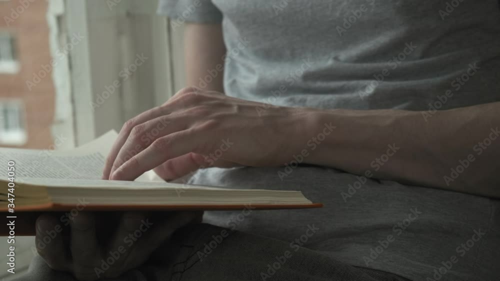 closeup on young man hands leafing through book. Activity, hobby during quarantine of coronavirus pandemic COVID-19, 2019-nCoV. self isolation leisure, stay home. male sits on windowsill, reads novel closeup on young man hands leafing through book. Activity, hobby during quarantine of coronavirus pandemic COVID-19, 2019-nCoV. self isolation leisure, stay home. male sits on windowsill, reads novel