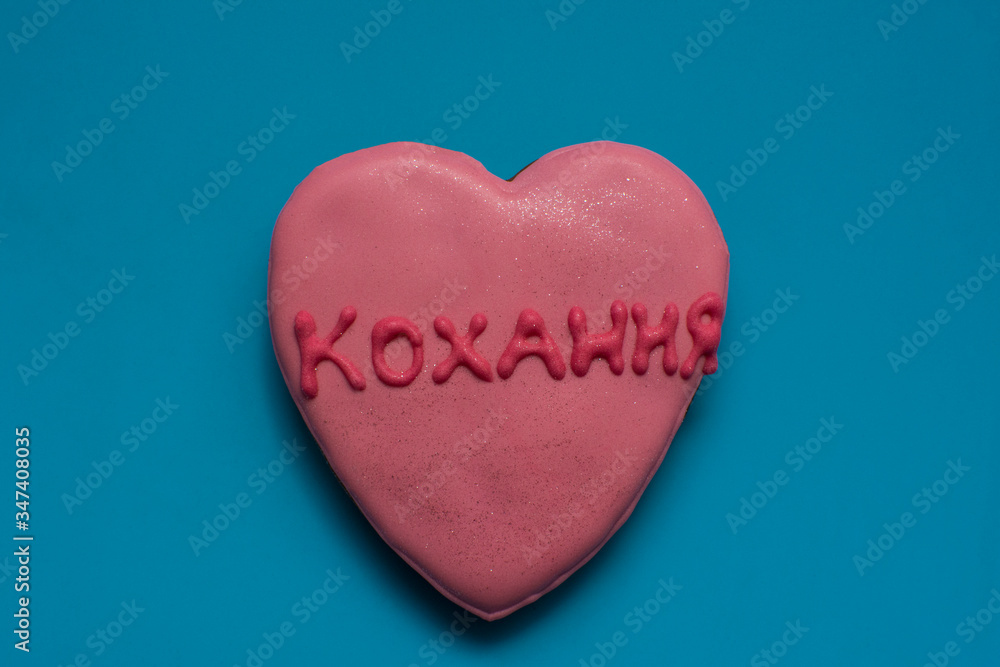 Fototapeta premium Pretty homemade gingerbread in the shape of a heart and with word - love, written in ukrainian language, on the bright blue background. Closeup.