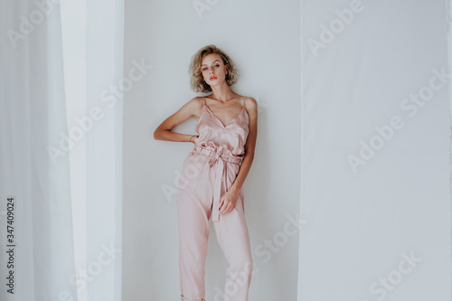 Beautiful fashionable blonde woman in pink clothes poses in white room