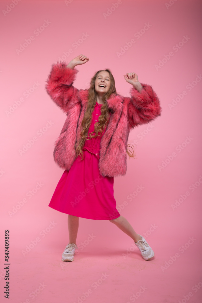 Beautiful young girl in a fashionable fur coat with pink fur, a pink dress and white gym shoes is dancing. Beautiful young girl in a fashionable fur coat with pink fur, a pink dress and white gym shoes is dancing.