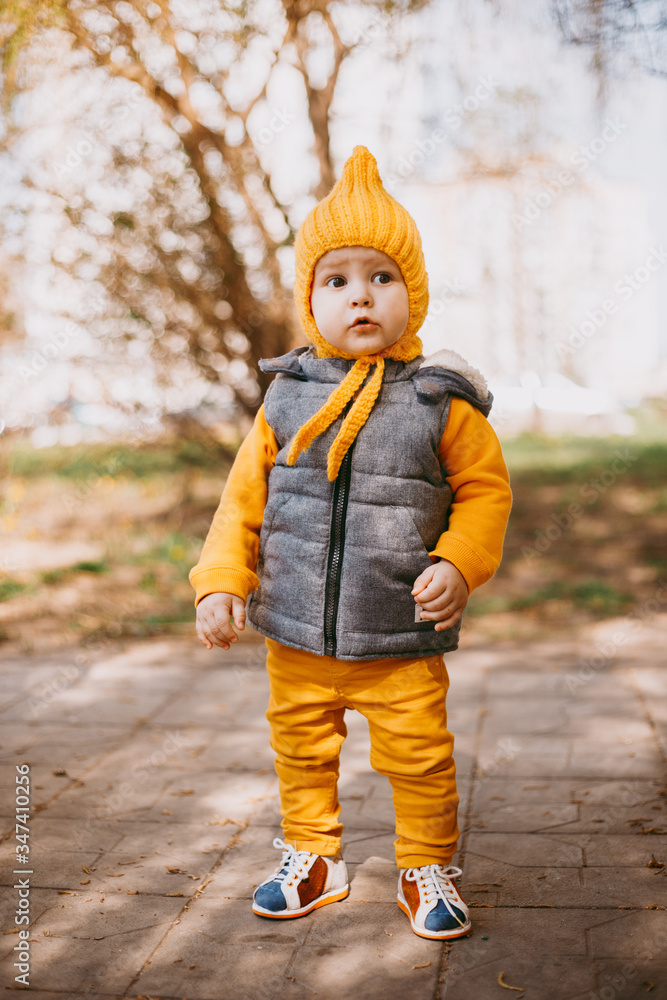 Stylish little one-year-old boy in a yellow hat, yellow pants and a gray jelly Stylish little one-year-old boy in a yellow hat, yellow pants and a gray jelly