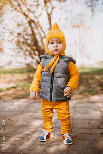 Fototapeta Naklejka Na Ścianę i Meble -  Stylish little one-year-old boy in a yellow hat, yellow pants and a gray jelly