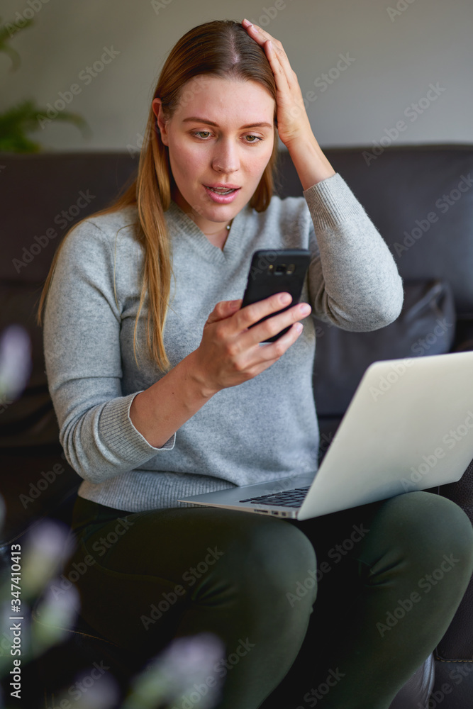 Sad woman sitting on sofa with laptop and talking on phone at home. College student studying on laptop and using phone. Sad woman sitting on sofa with laptop and talking on phone at home. College student studying on laptop and using phone.