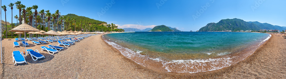 Panorama of a sandy beach without people and with sun loungers, umbrellas, palm trees, Marmaris,