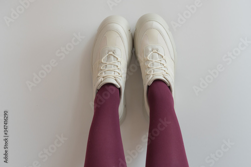 Legs in red tights, lifted up. Fashionable modern shoes with a massive sole. White sneakers and red tights.