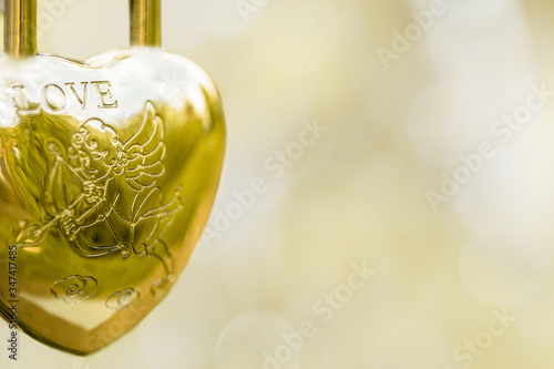 Hinged gold lock in the form of a heart, the inscription love angel with an arrow on a blurred background. Symbol of wedding. Copy space.