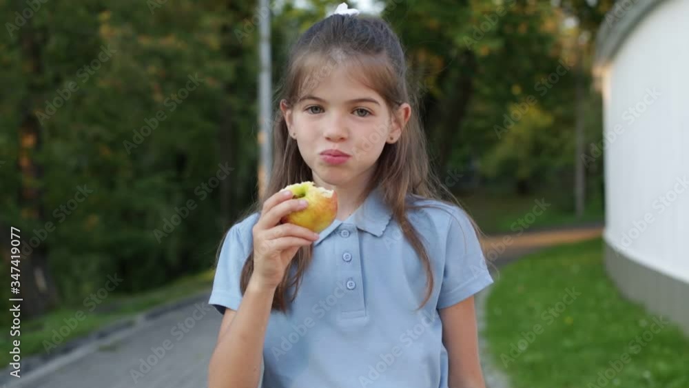 Little beautiful school girl with a backpack in a school uniform eats an apple in the park. Little beautiful school girl with a backpack in a school uniform eats an apple in the park.