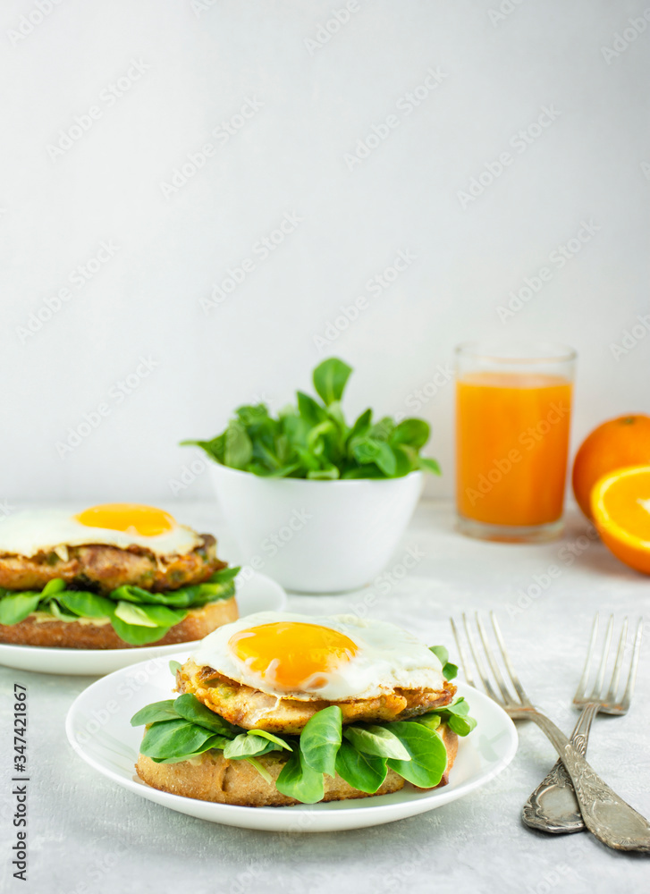 European breakfast Sandwich with fried egg, chicken, herbs and orange juice. A sandwich. Breakfast on a light table, side view.