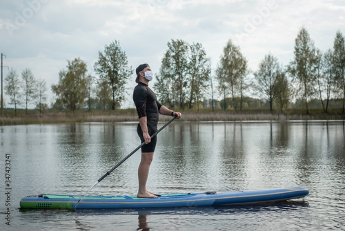 sports man in a medical mask rowing a paddle standing on a Board, prevention of covid,