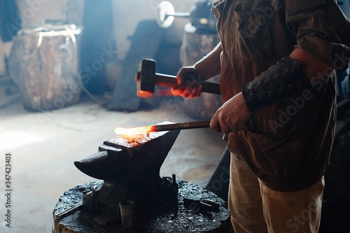Blacksmith working metal with hammer on the anvil in the forge