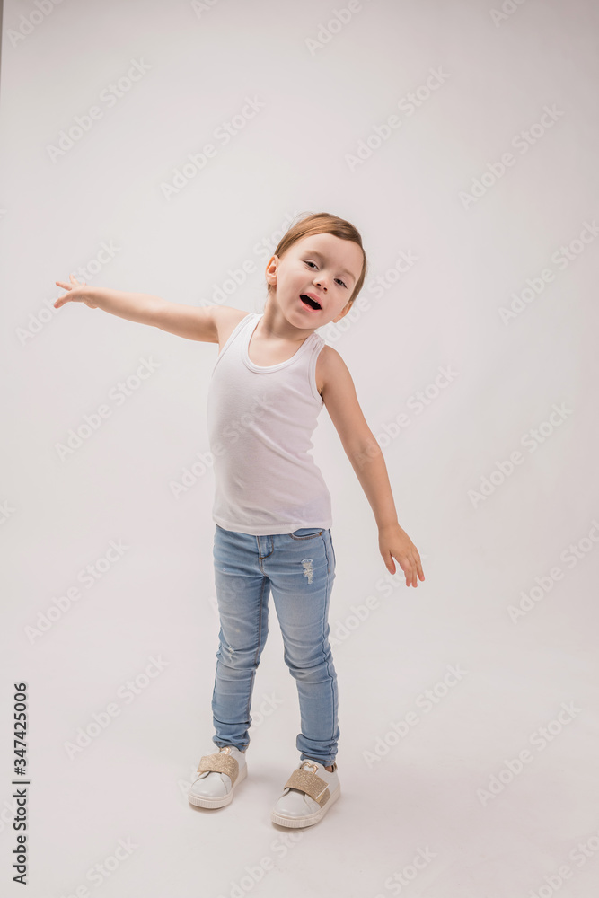 The little girl spread her arms out on the white background. Flight simulation. Cute girl in a white top and jeans. Full-length portrait. The little girl spread her arms out on the white background. Flight simulation. Cute girl in a white top and jeans. Full-length portrait.