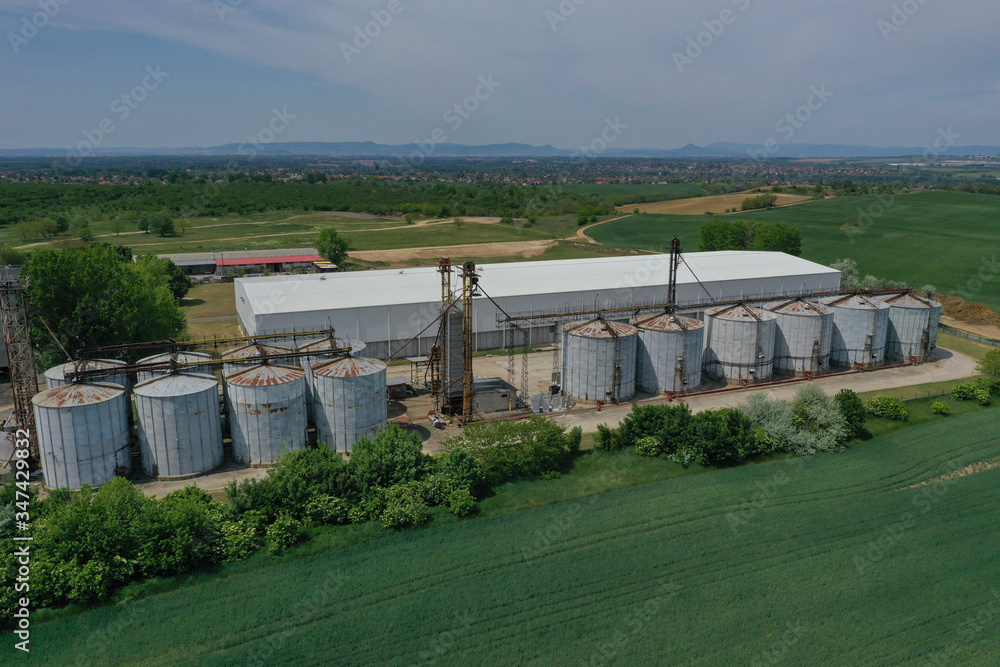 Aerial view with drone, agricultural silo, next to wheat or barley field - industrial elevator dryers, building exterior, storage and drying of cereals, wheat, corn, soybeans, sunflowers. In Europe