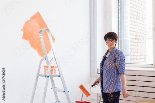 Renovation, redecoration and repair concept - middle-aged woman painting wall in new home.