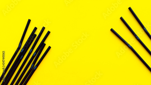 Black plastic tubes for juice and cocktails are scattered on a yellow background. Disposable straws. The subject of serving. Bar accessories. Summer planet pollution concept.