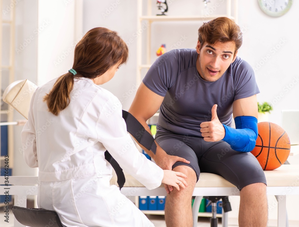 Fototapeta premium Handsome basketball player visiting female doctor traumatologist