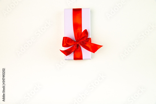 Holiday gift box with a red ribbon bow isolated on a beige background.