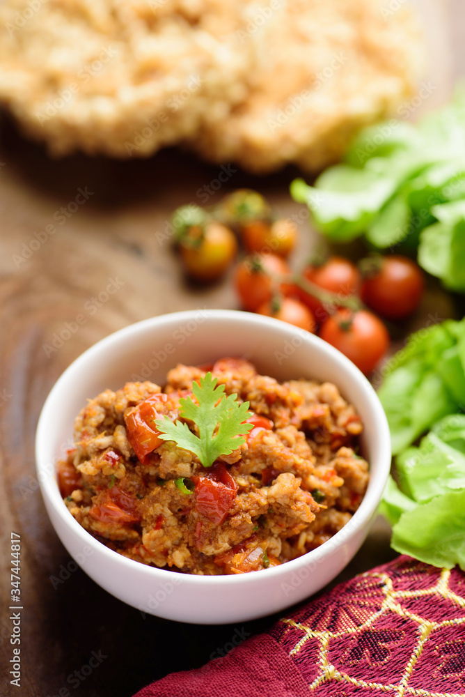Northern Thai food (Nam Prik Ong), spicy chili minced pork with tomatoes in a bowl on wooden table eating with vegetables, Thai chili paste Northern Thai food (Nam Prik Ong), spicy chili minced pork with tomatoes in a bowl on wooden table eating with vegetables, Thai chili paste
