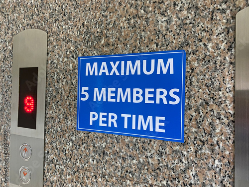 A sign warning message which has content is maximum five members per time is placed on a wall beside the elevator in an office during the pandemic of covid-19
