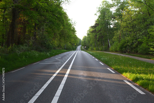 Empty rural road with clear white lines in a wooded area, at the right a path for bicycles