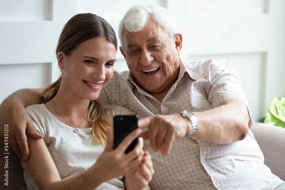 Happy mature 90s father and millennial girl child sit on couch smile making self-portrait picture on cell together, overjoyed senior dad and adult daughter have fun take selfie on smartphone at home Happy mature 90s father and millennial girl child sit on couch smile making self-portrait picture on cell together, overjoyed senior dad and adult daughter have fun take selfie on smartphone at home