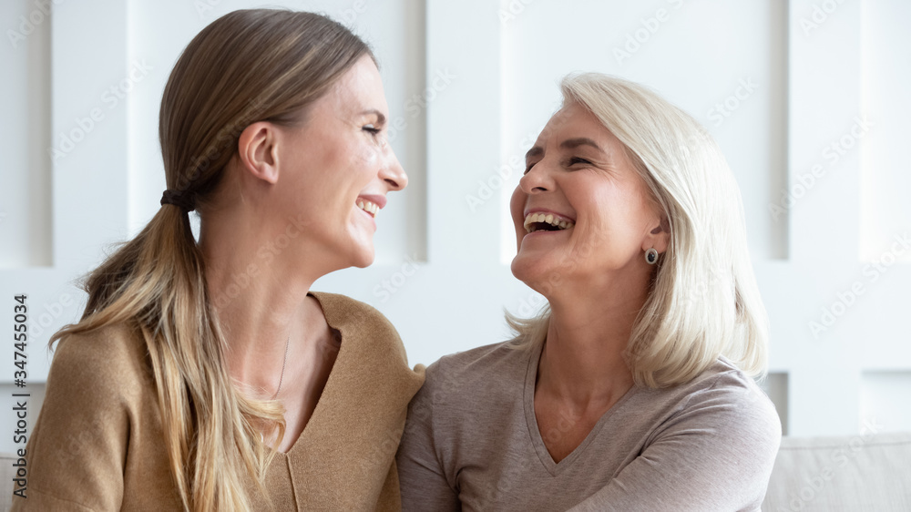 Happy senior mom and grownup daughter sit relax on couch talking laughing at home, smiling middle-aged mother and adult millennial girl rest have fun chatting enjoying weekend together Happy senior mom and grownup daughter sit relax on couch talking laughing at home, smiling middle-aged mother and adult millennial girl rest have fun chatting enjoying weekend together