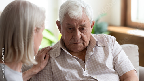 Caring senior woman touch support upset distressed elderly 80s husband mourning or yearning on couch in retirement house, loving mature wife comfort caress depressed old thoughtful unhappy husband