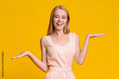 Joyful girl in summer dress demonstrating something on her empty palms