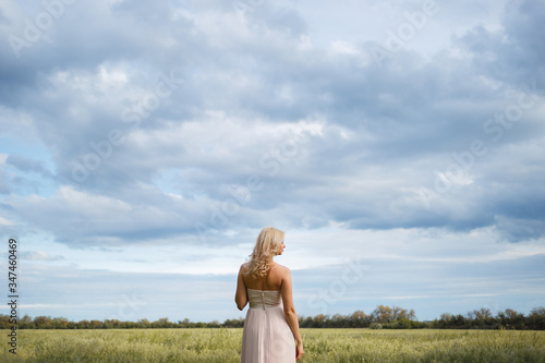 Woman stands in the middle of a green field and a blue sky with clouds