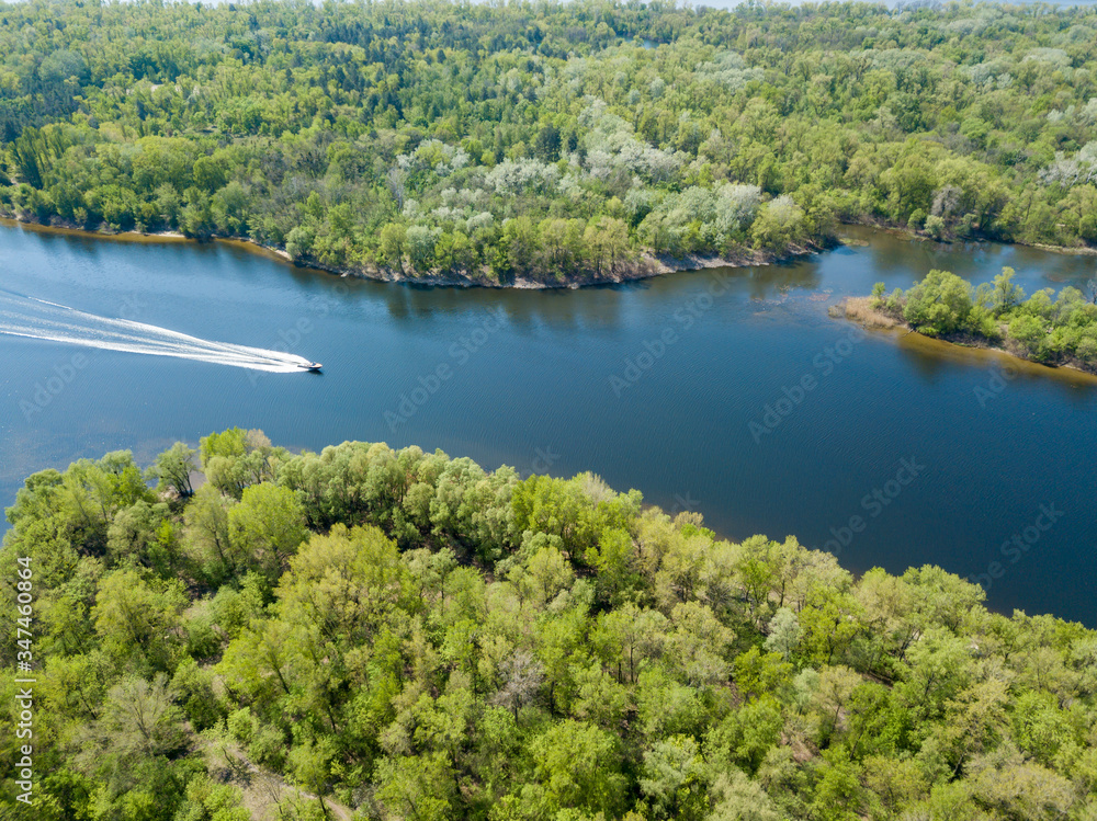 A motor boat floats on the Dnieper River in Kiev. Green trees on the banks of the river. Sunny spring day. A motor boat floats on the Dnieper River in Kiev. Green trees on the banks of the river. Sunny spring day.