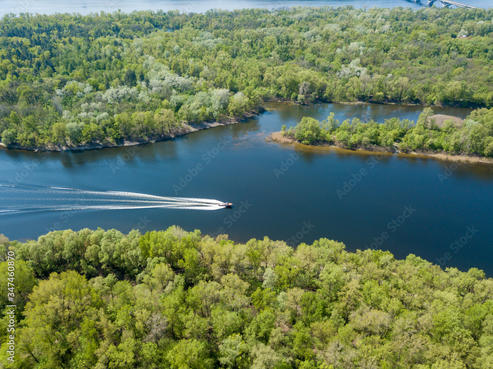 Obraz premium A motor boat floats on the Dnieper River in Kiev. Green trees on the banks of the river. Sunny spring day.