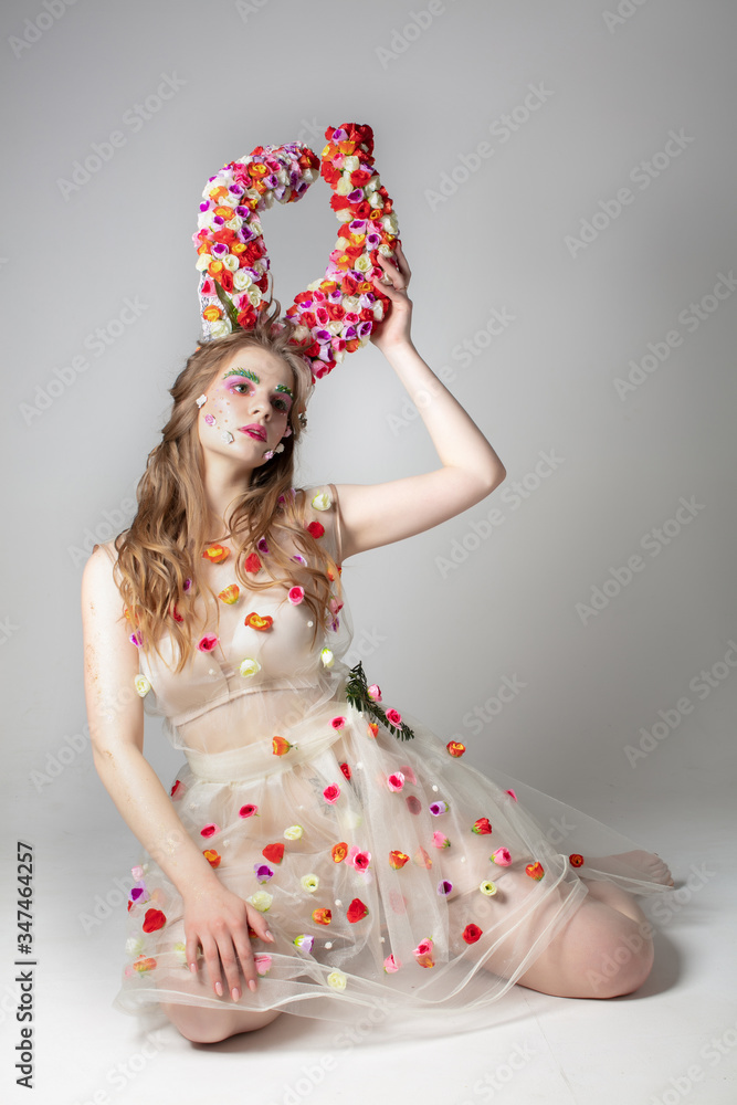 Fantastic girl model with floral horns on a studio background. Maleficent. Spring or summer beauty. Woman in the image of a flower.