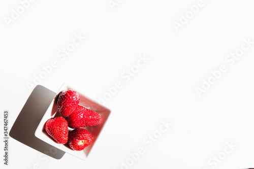 Minimal view of a bowl of red strawberry over flat white background and copy space