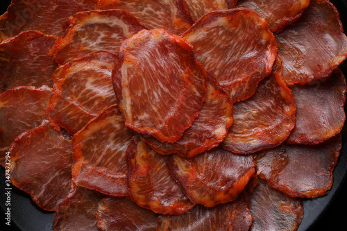 Close-up (detail) of a portion of acorn-fed Iberian loin on a black plate on a black background