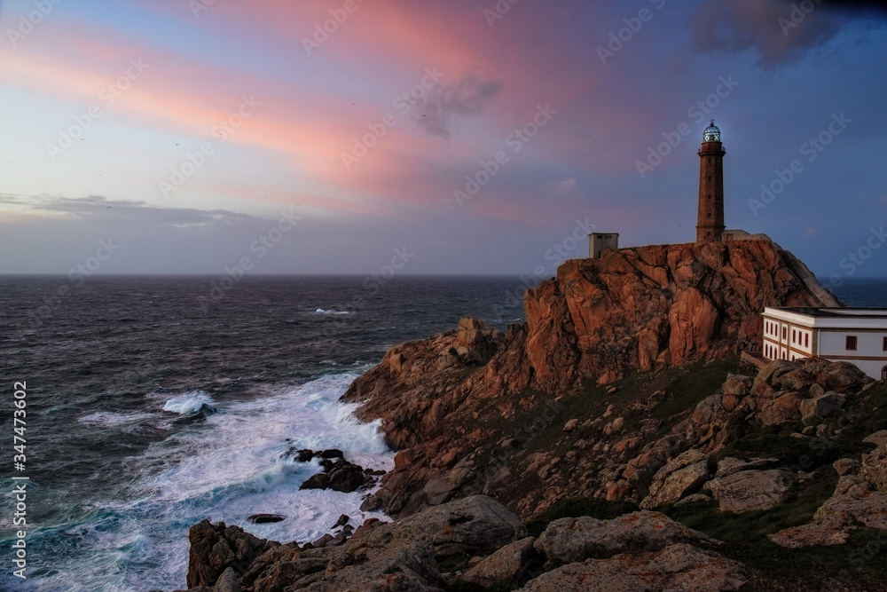 Lighthouse at Cabo Vilan on the Galician coast in a colourful sunset and with the sea in a rage. The oldest electric lighthouse in Spain. Galicia, Spain.