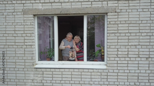 Old grandparents couple cooking barbecue on electric grill on windowsill at home