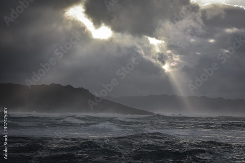 Big waves break on the coast, in the sunlit sea, passing through the clouds at sunset. Galicia, Spain.