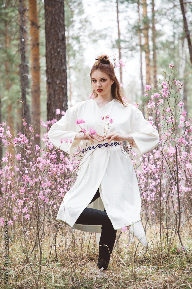 A girl dressed in Japanese style in a flowering forest among pink flowers A girl dressed in Japanese style in a flowering forest among pink flowers