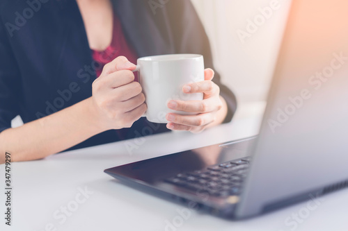 Life style people concept: Hands of woman hold a white mug of coffee in front of notebook