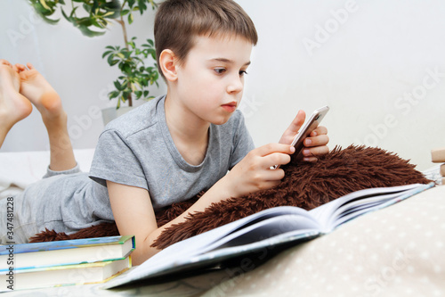 A boy with a smartphone in his hands next to books in bed teaches lessons. Distance learning online over the Internet photo