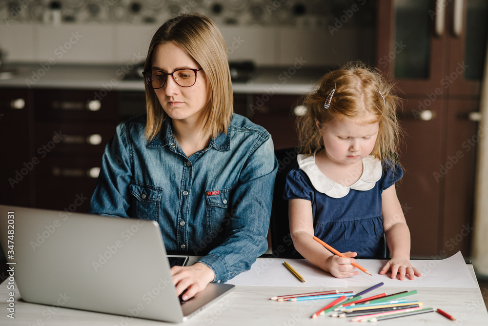 Woman working, learns on laptop computer. A young mother on a childcare leave works at home with daughter play and paint. Freelance. Writing, typing. Communication and technology concept. Paperwork. Woman working, learns on laptop computer. A young mother on a childcare leave works at home with daughter play and paint. Freelance. Writing, typing. Communication and technology concept. Paperwork.