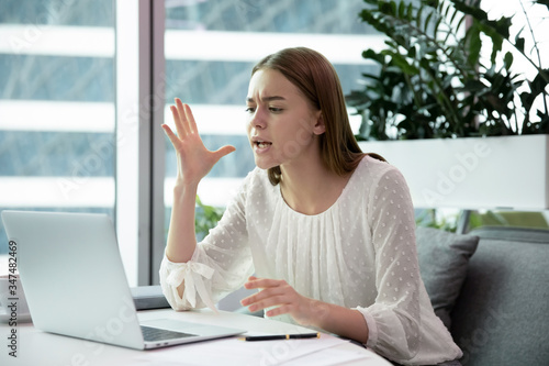 Stressed angry businesswoman having problems with computer crash feels annoyed swears on a slow device sitting at modern office room alone, broken laptop failure, need repair, unsaved lost information