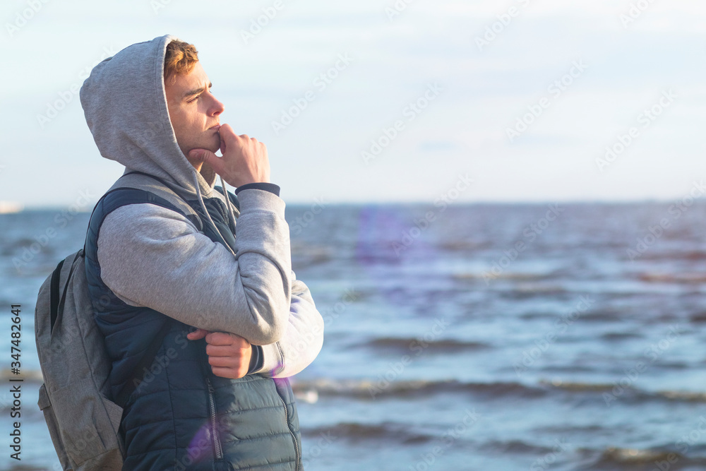 Pensive young man on the background of the bay. Handsome romantic guy is dreaming on the background of the sea. Copy Space