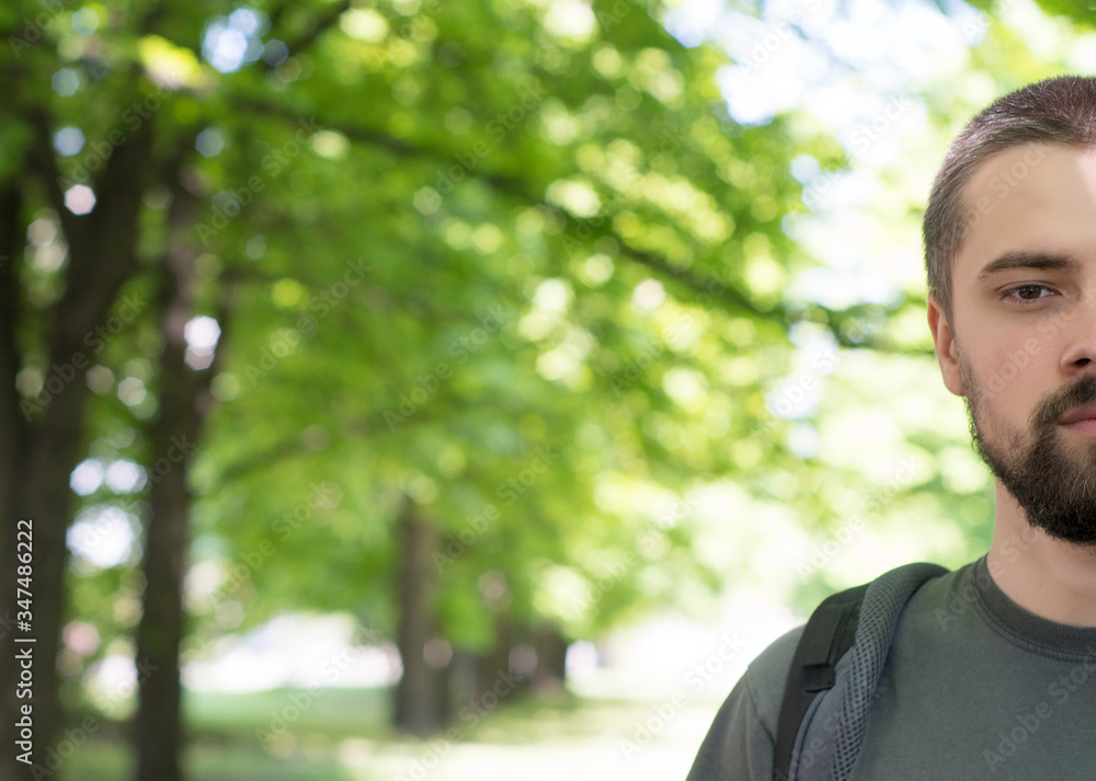 Manly young tourist man with a backpack looks at the camera. Close-up of half face. Nature travel concept with place for text. Manly young tourist man with a backpack looks at the camera. Close-up of half face. Nature travel concept with place for text.