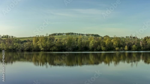 Side move Timelapse of calm lake surface with views of surrounding countryside full of hills stomas during a sunny day white clouds in sky reflecting on the water surface Hustopece Czech Republic photo